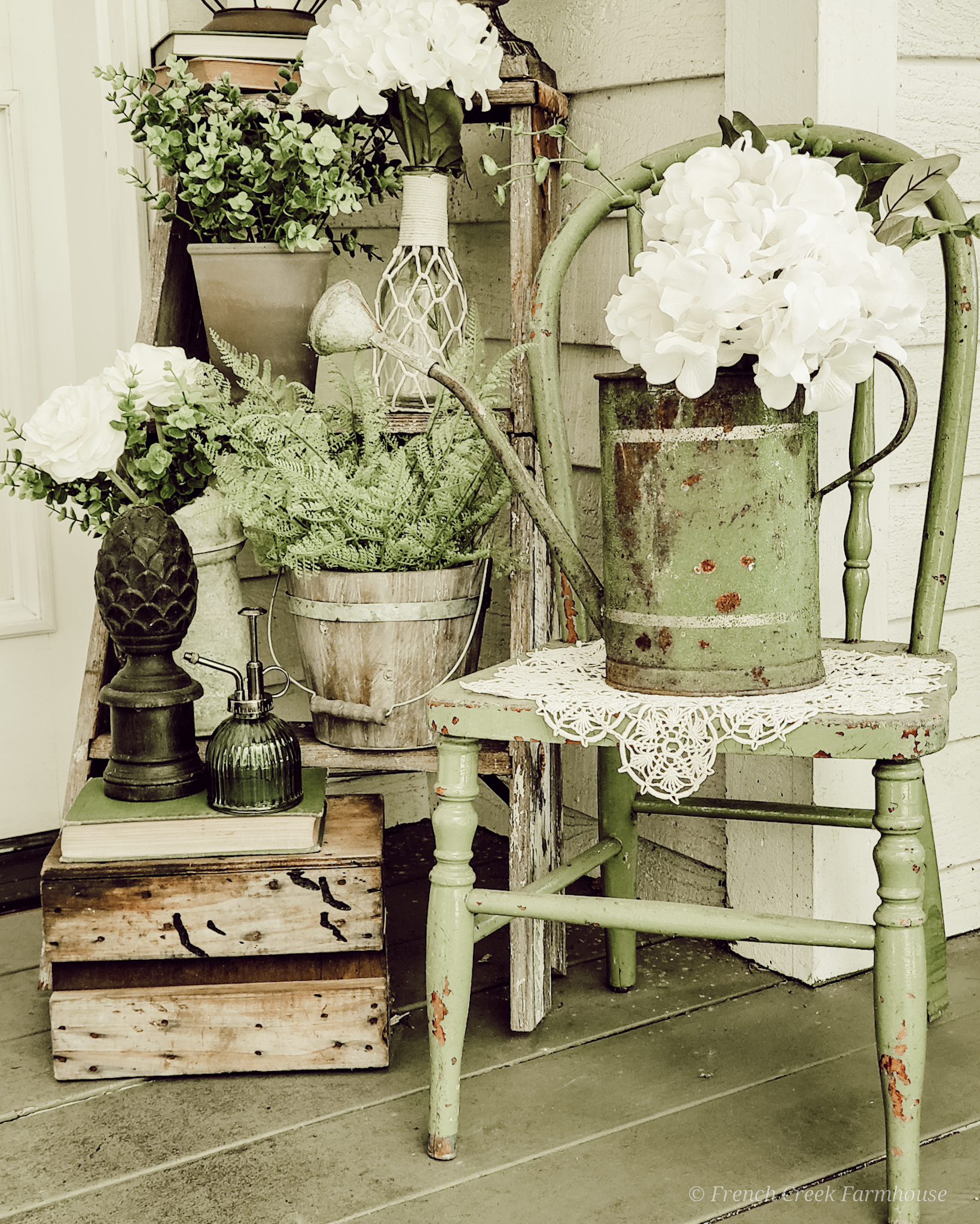 This springtime front porch vignette features a vintage watering can, chippy green chair, rustic old stepladder, and loads of spring florals