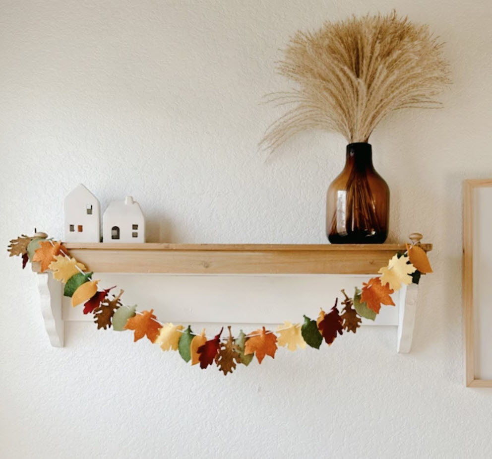 A garland of autumn leaves made from felt strung across a wood shelf