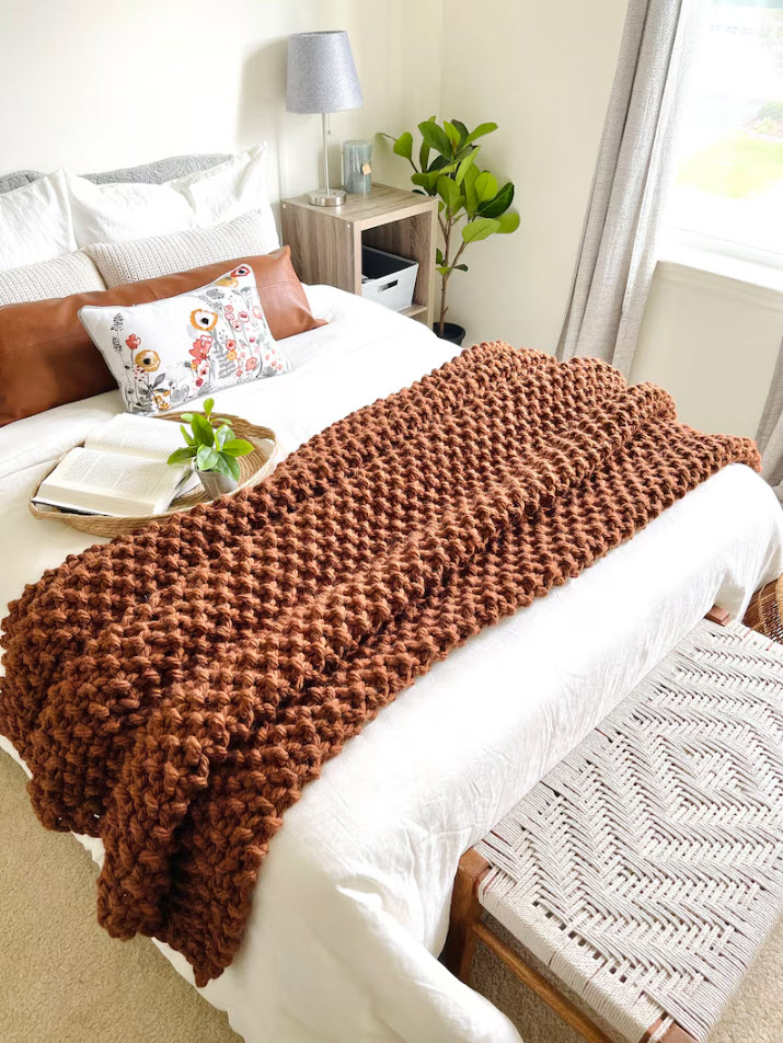 Orange chunky knit blanket on a white duvet covered bed